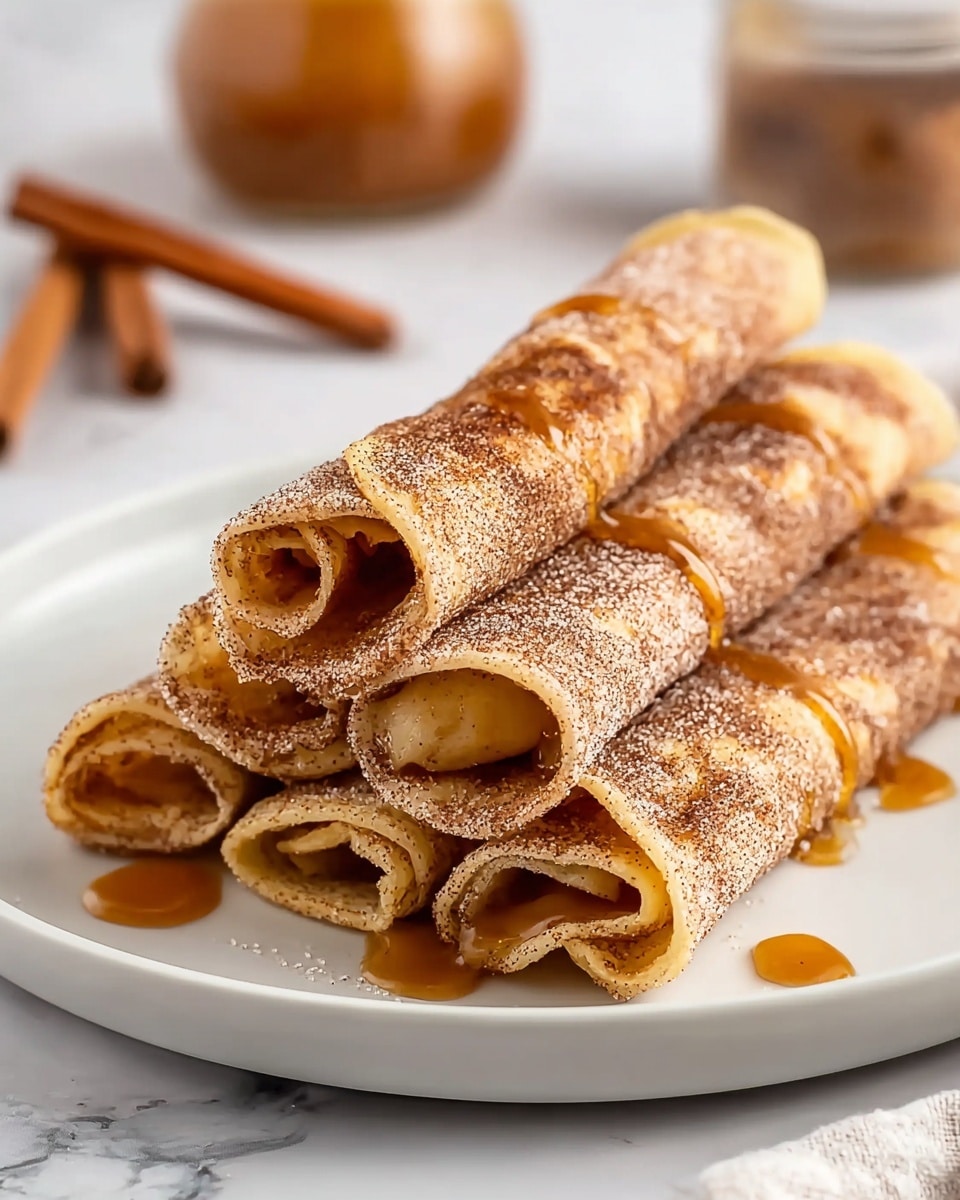 A stack of five rolled crepes sits on a white plate placed on a white marbled surface, each crepe coated with a fine layer of cinnamon sugar that gives a speckled brown texture. The crepes are rolled tightly, showing soft, golden-brown edges with a slight crispness. Caramel sauce is drizzled over the top, with some of it oozing out from the ends and pooling on the plate, adding a glossy amber shine. In the blurred background, two cinnamon sticks and a small jar of caramel sauce subtly complete the scene. photo taken with an iphone --ar 4:5 --v 7