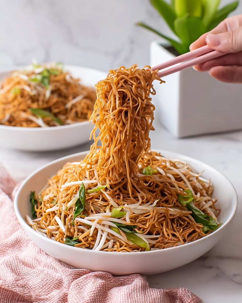 A white bowl filled with thin, brownish-orange noodles mixed with long, white bean sprouts and some green leafy vegetables. A woman's hand is using pink chopsticks to lift a generous clump of noodles above the bowl, showing their texture and slight shine. In the background, another white bowl is partially visible, also filled with the same noodles. The whole scene is set on a white marbled surface with a small green plant in a white rectangular pot behind the bowl, and a soft pink and white checkered cloth in the foreground. Photo taken with an iphone --ar 4:5 --v 7