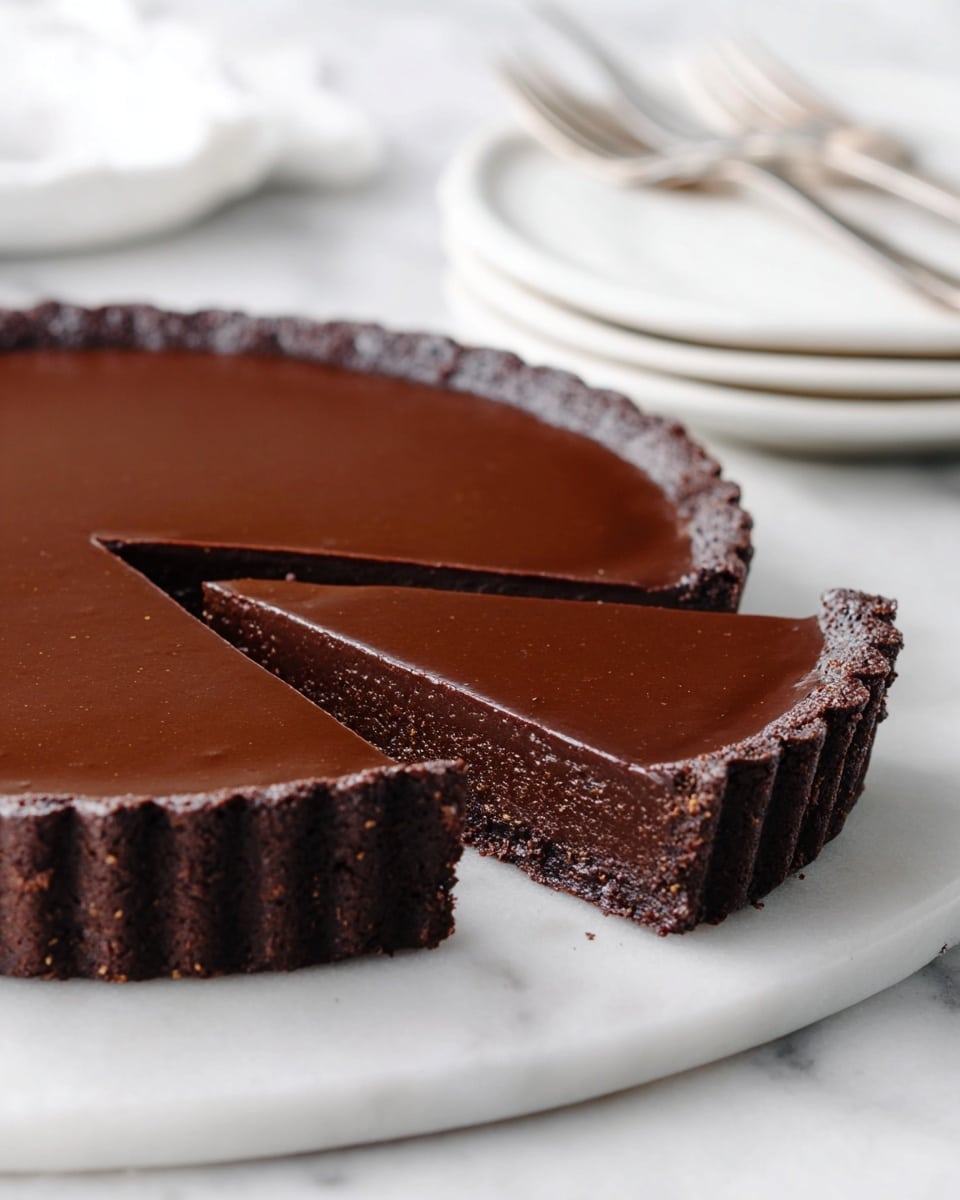 A rich chocolate tart is shown with a large round shape, featuring a thick, smooth, and shiny dark chocolate top layer. Below the top is a dense, creamy milk chocolate filling, which sits above a firm, crumbly chocolate crust forming the base and sides of the tart. One slice is cut and placed on a white plate with small brown spots, accompanied by a silver fork on the right side of the slice. The whole tart rests on a white marbled surface in the background, with a soft, neutral tone behind it. photo taken with an iphone --ar 4:5 --v 7