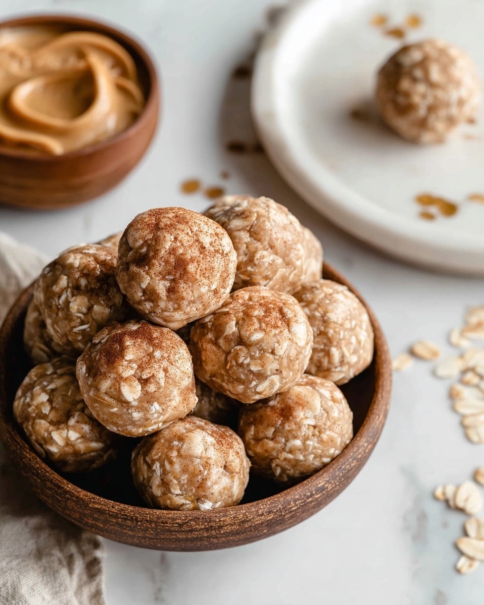 A brown bowl filled with round energy bites made with visible oats on their surfaces, some with a light dusting of cinnamon on top; the energy bites are light beige in color with a slightly sticky texture, piled above the bowl's edge. Nearby, on a white plate, there is another energy bite, and in the background, a round white bowl holds smooth peanut butter inside a wooden cup, all set on a white marbled surface with faint gold leaf patterns. photo taken with an iphone --ar 4:5 --v 7