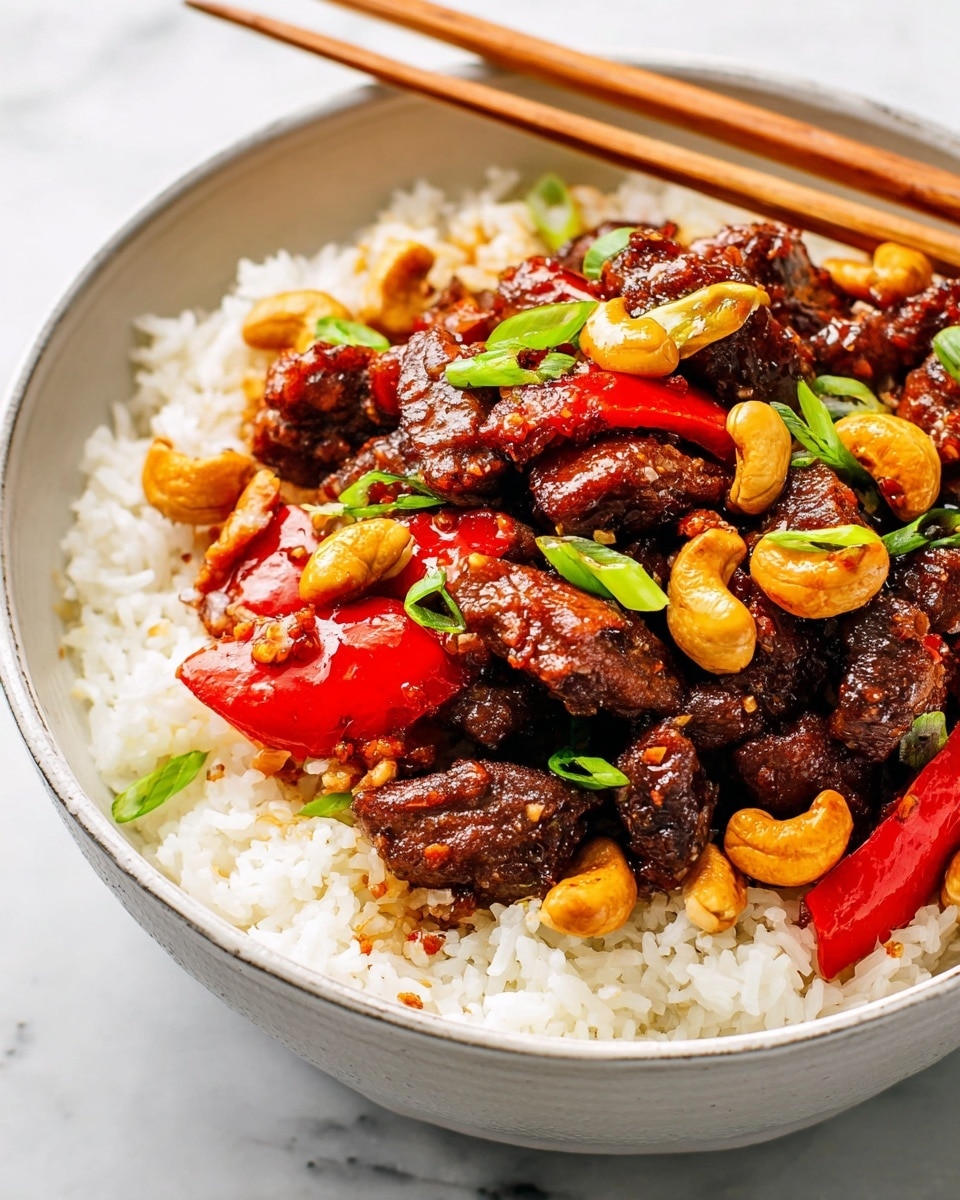 A white bowl filled with a base layer of fluffy white rice, topped with pieces of dark brown, glossy stir-fried meat coated in a shiny sauce. Mixed with the meat are bright red slices of bell pepper and golden toasted cashew nuts. Small pieces of green onion are scattered on top, adding a pop of fresh green color. A pair of wooden chopsticks rests across the rim of the bowl, which sits on a white marbled surface. photo taken with an iphone --ar 4:5 --v 7