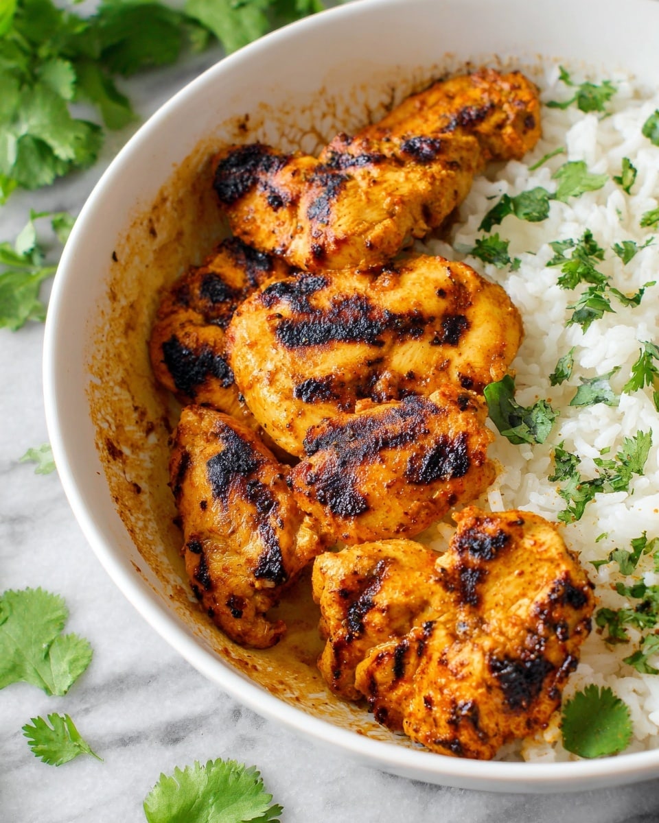 A white bowl filled with several pieces of grilled chicken that are golden brown with dark char marks, arranged on the left and center side, showing a slightly crispy texture. On the right side of the bowl, there is a layer of white rice with a fluffy texture, some sprinkled green cilantro leaves are spread across the chicken and rice, adding bright green color. The bowl is placed on a white marbled surface with some fresh cilantro leaves scattered nearby. Photo taken with an iphone --ar 4:5 --v 7