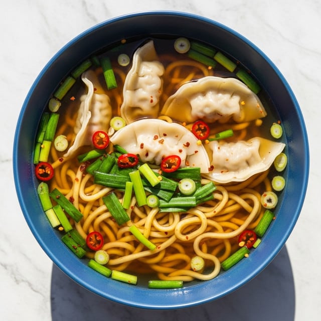 A blue bowl filled with clear brown broth holds pale, soft dumplings floating on top. Yellowish thick noodles twist around the bowl underneath, mixed with bright green sliced scallions scattered throughout. Small red chili flakes add specks of color on the dumplings and broth surface. The bowl sits on a white marbled texture, with natural light casting a shadow on one side. photo taken with an iphone --ar 4:5 --v 7