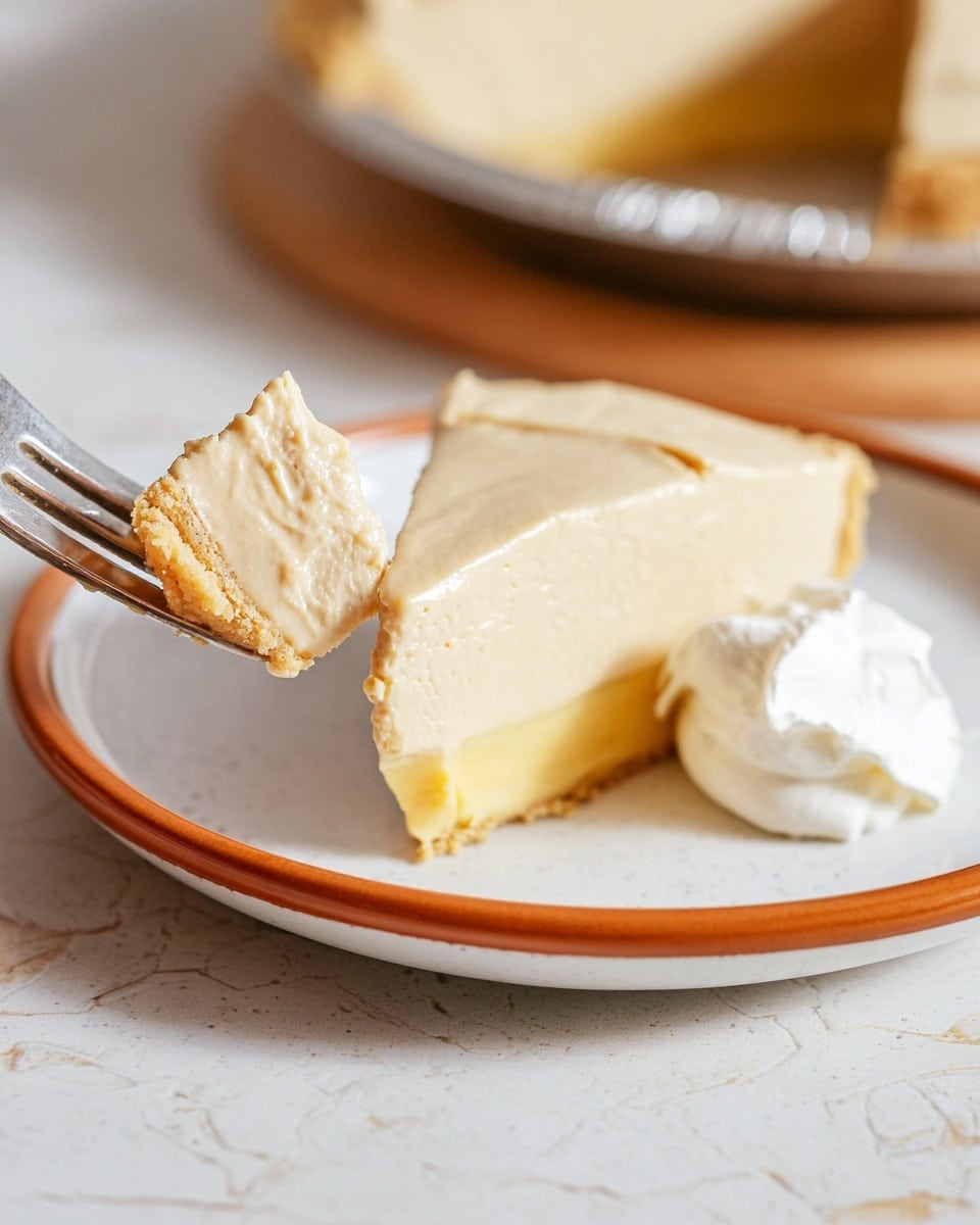 A slice of creamy beige pie with a thick smooth filling and a light yellow crust at the bottom sits on a white plate with an orange rim. A piece of the pie, showing two layers—the yellow crust base and the beige filling top—is held up close by a fork on the left side. The pie slice on the plate has a dollop of white whipped cream on its top right corner. The surface underneath the plate is a white marbled texture. Photo taken with an iphone --ar 4:5 --v 7