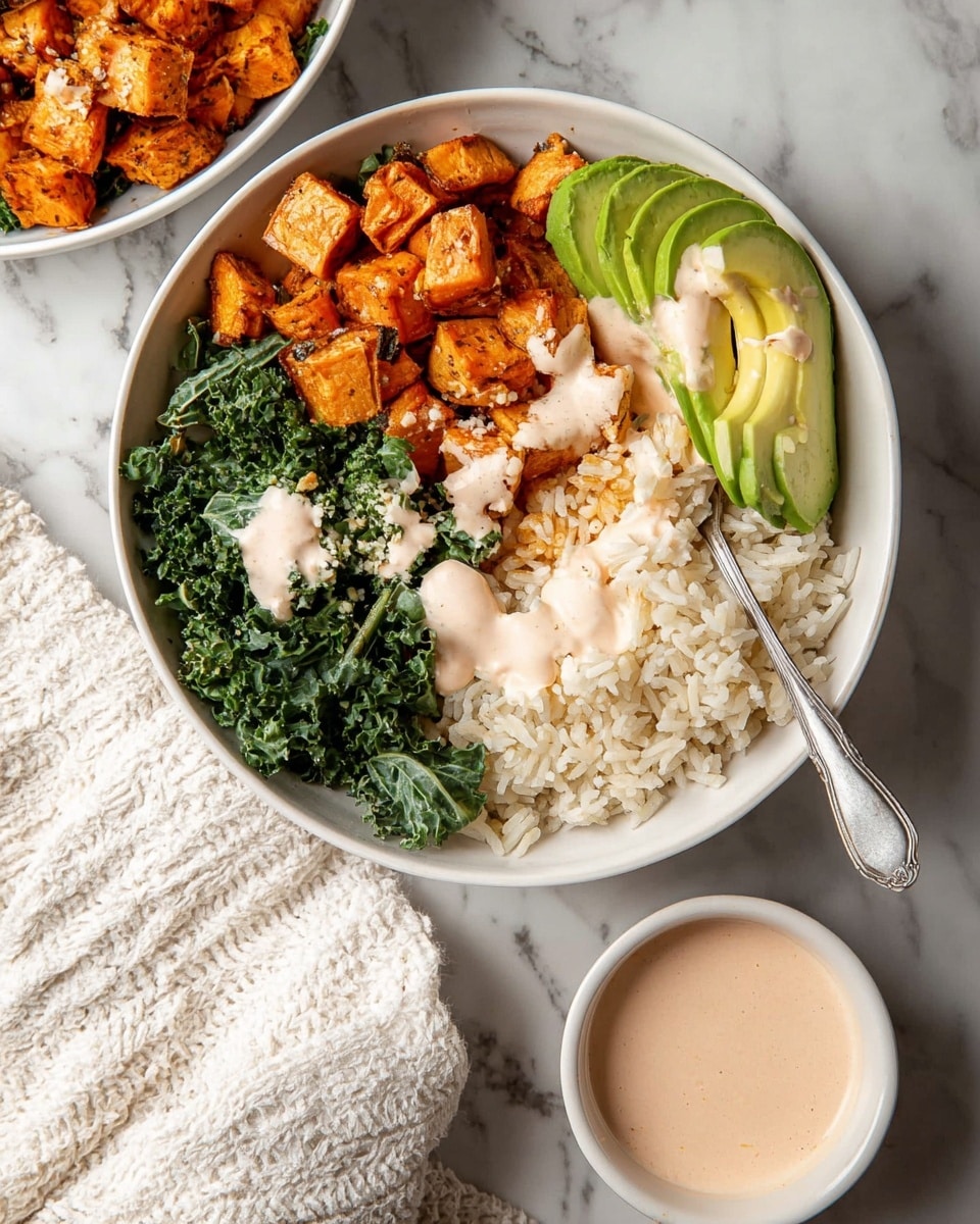 A white bowl filled with four main layers arranged side by side: on the left, golden-brown roasted sweet potato chunks showing a slightly crispy texture, next to it a dark green leafy kale with a fresh, rough texture, then a fan of smooth, light green avocado slices, and on the right, a heap of fluffy white rice topped lightly with a creamy pale pink sauce that is also drizzled over the sweet potatoes and kale. A silver spoon rests in the rice portion with some sauce on it. Below the bowl is a small white bowl filled with more of the pale pink sauce with a spoon inside. The background is a white marbled texture with a white textured towel nearby. photo taken with an iphone --ar 4:5 --v 7