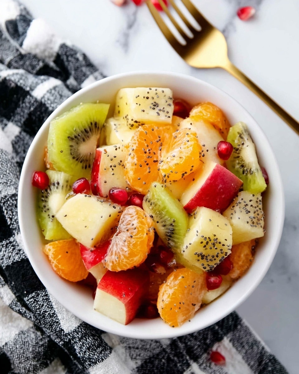 A white bowl filled with a fresh fruit salad showing multiple colorful layers: bright orange tangerine segments, green kiwi slices, yellow banana coins coated with small black seeds, red apple cubes with their skin on, and scattered red pomegranate seeds. The fruit pieces have a shiny, juicy look with poppy seeds sprinkled over them. The bowl sits on a black and white checkered cloth, resting on a white marbled surface, next to a gold fork. Photo taken with an iphone --ar 4:5 --v 7