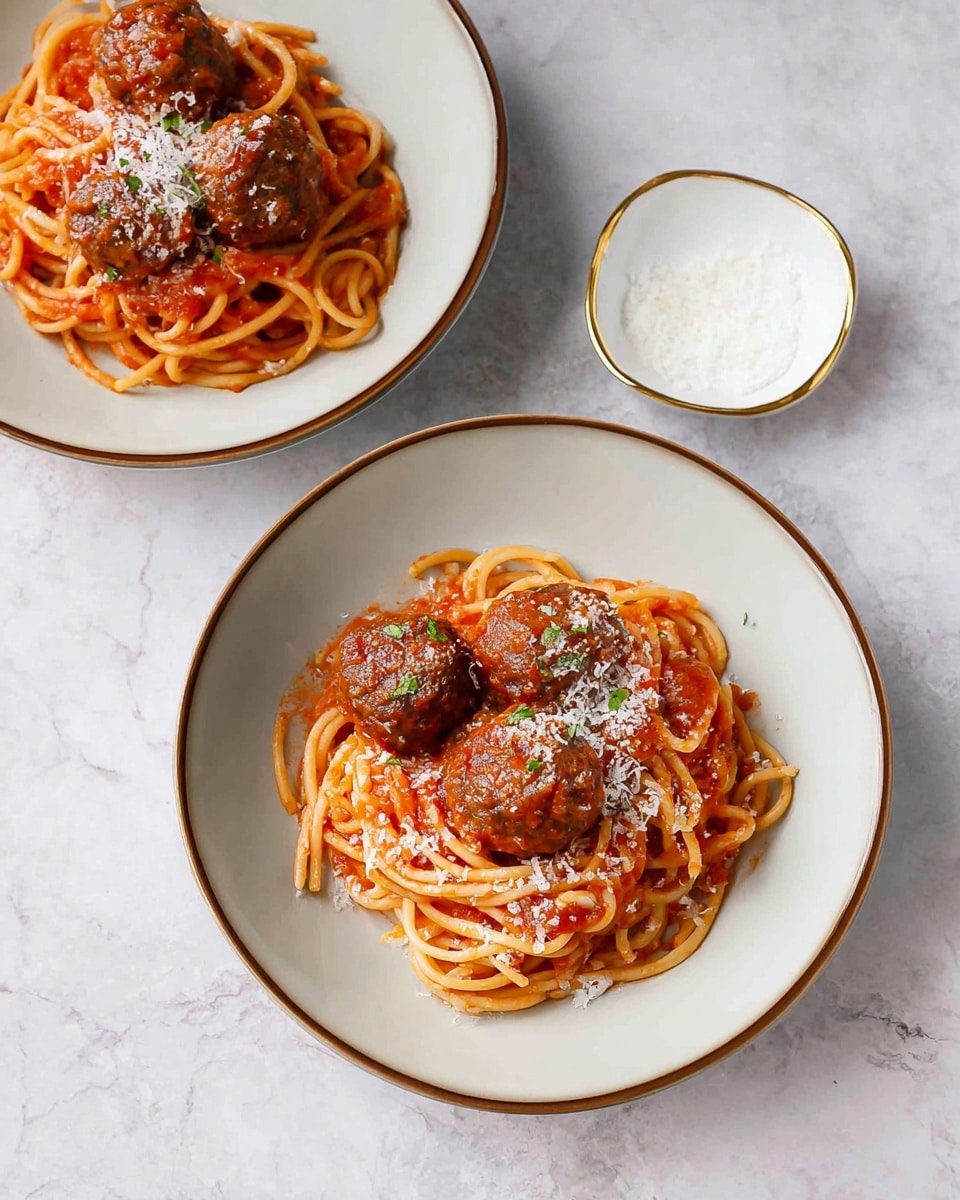 Two white bowls with brown rims are filled with spaghetti pasta coated in red tomato sauce. Each bowl has three round brown meatballs on top of the pasta, sprinkled with finely grated white cheese. The bowls are placed on a white marbled surface. A small white bowl with gold trim in the background contains coarse white salt. photo taken with an iphone --ar 4:5 --v 7