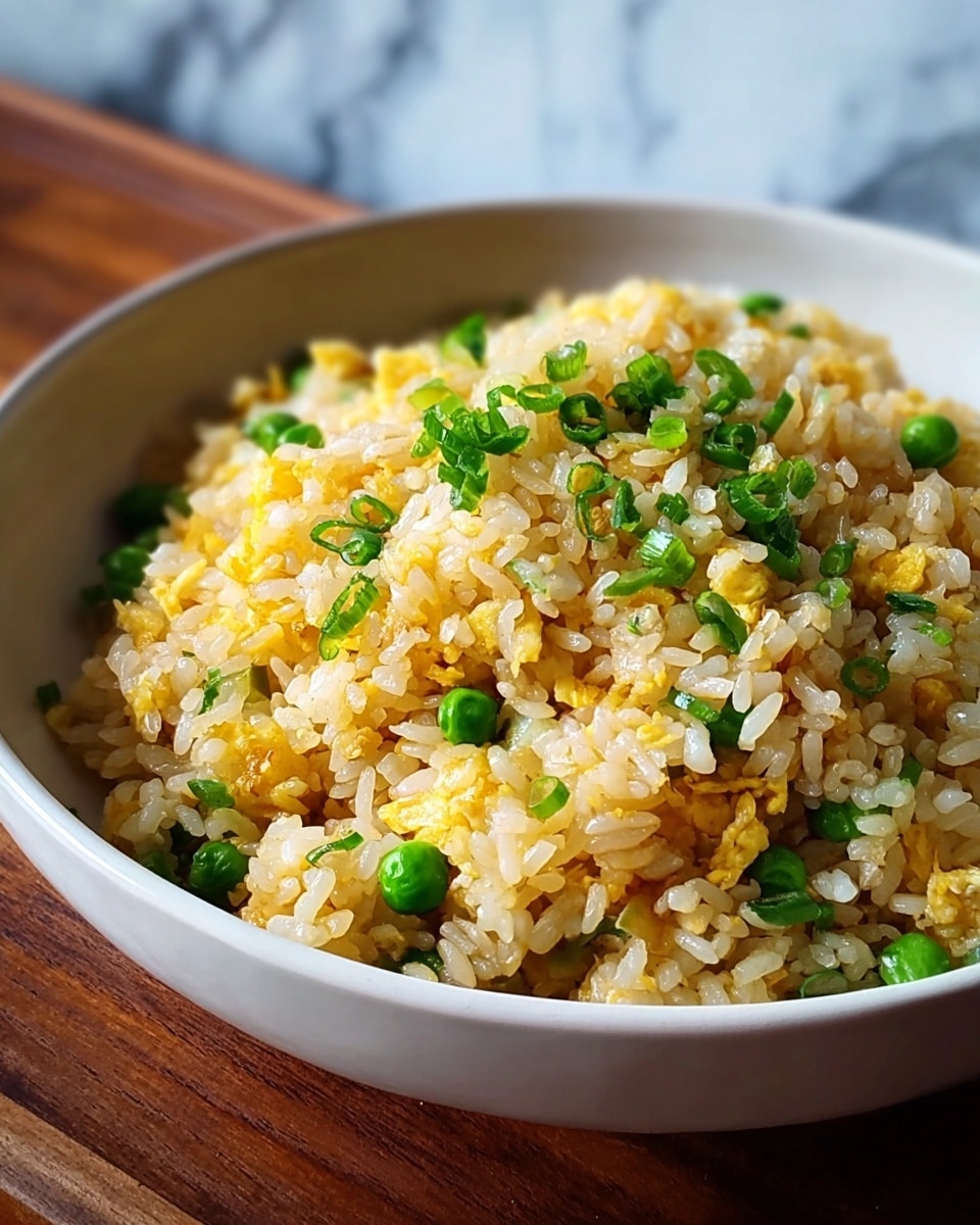 The image shows a close-up of a bowl of fried rice. The rice is light golden yellow with small green peas and chopped green onions mixed evenly throughout. The texture appears fluffy with visible grains of rice, small golden scrambled egg bits, and bright green vegetable pieces scattered on top and throughout the dish. The bowl is white and placed on a dark wooden surface with a blurred white marbled background behind it. photo taken with an iphone --ar 4:5 --v 7
