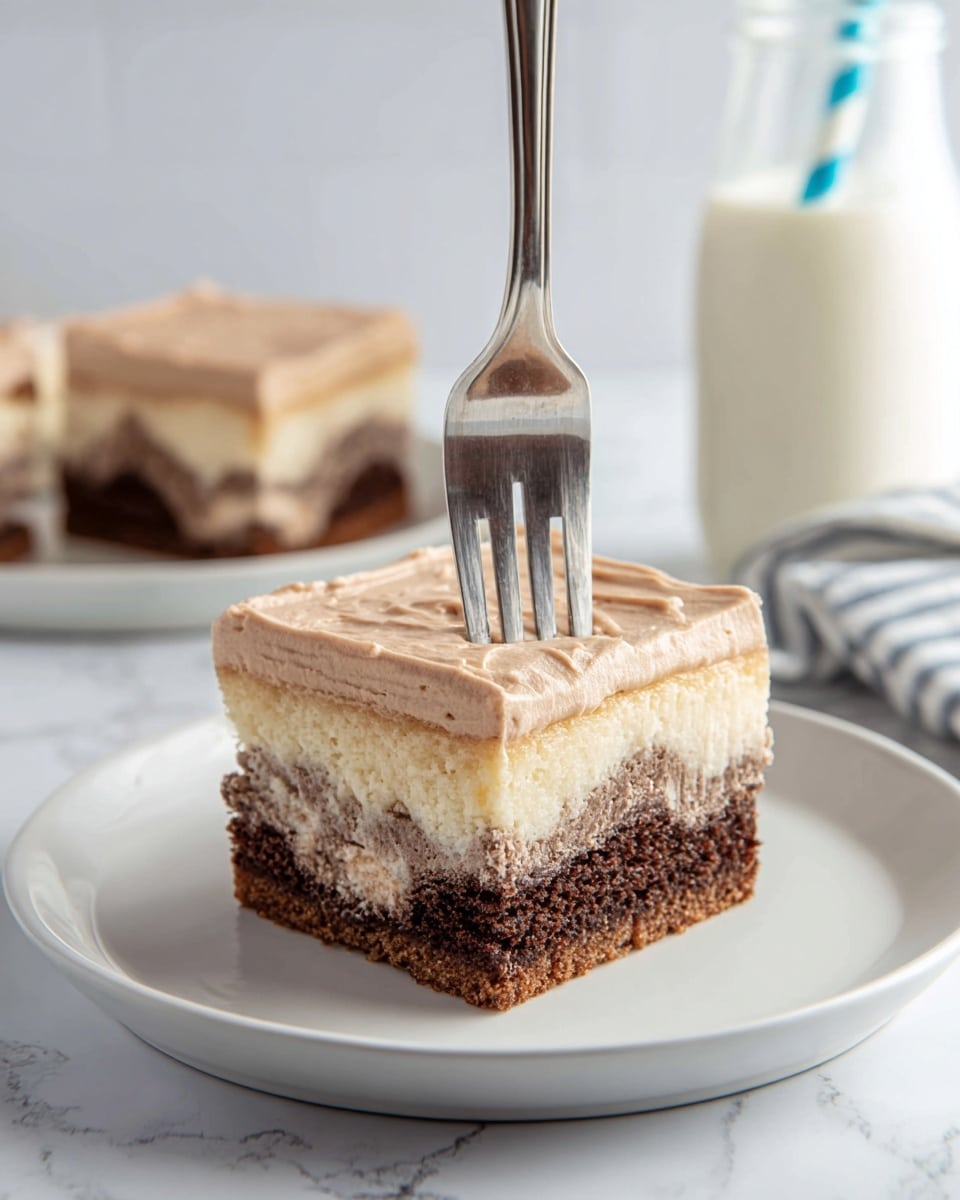 A square piece of cake with three layers sits on a white plate over a white marbled surface. The bottom layer is light cream with some brown swirls, the middle layer is dark brown and moist with a soft texture, and the top layer is a thick, light brown, smooth and fluffy frosting. A metal fork is pressed slightly into the frosting on the cake in the foreground, while a second piece of the same cake is blurred in the background on another white plate. A bottle of milk with a blue-striped straw is partly visible in the back. photo taken with an iphone --ar 4:5 --v 7
