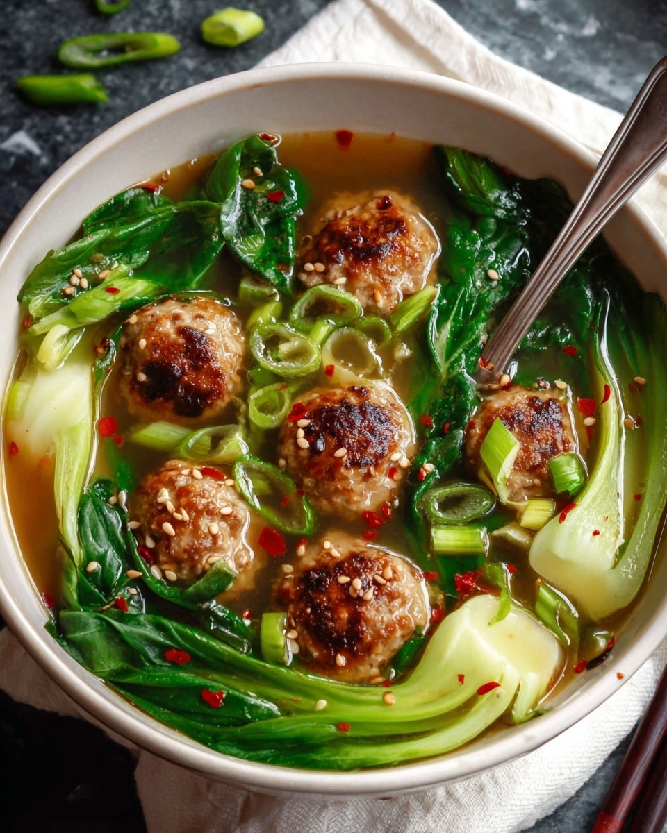 The image shows a white bowl filled with clear broth soup containing six browned meatballs floating among bright green bok choy leaves and sliced green onions. The soup has a few red chili flakes and white sesame seeds sprinkled on top, adding extra colors and textures. A silver spoon is partly inside the bowl resting on the edge. The bowl sits on a white marbled surface with a white napkin underneath and dark chopsticks next to it. Photo taken with an iphone --ar 4:5 --v 7
